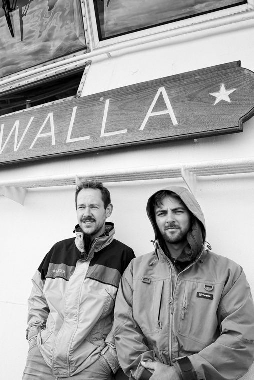 Black and white portrait of two men under a WALLA sign