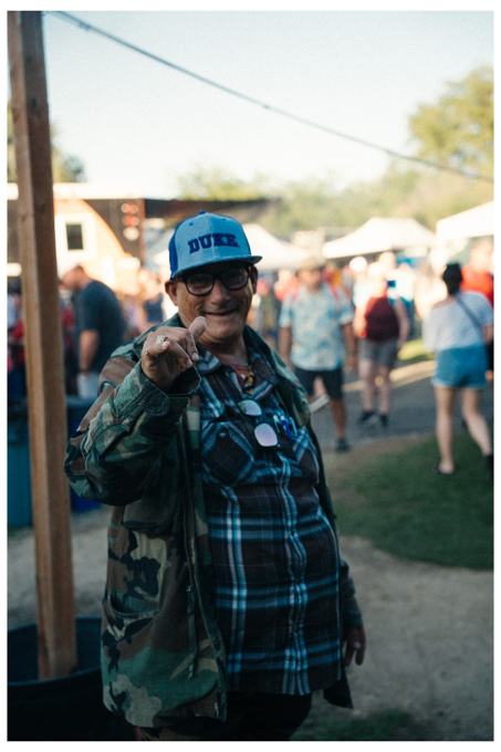 Smiling man in a Duke cap giving a thumbs up at an outdoor festival