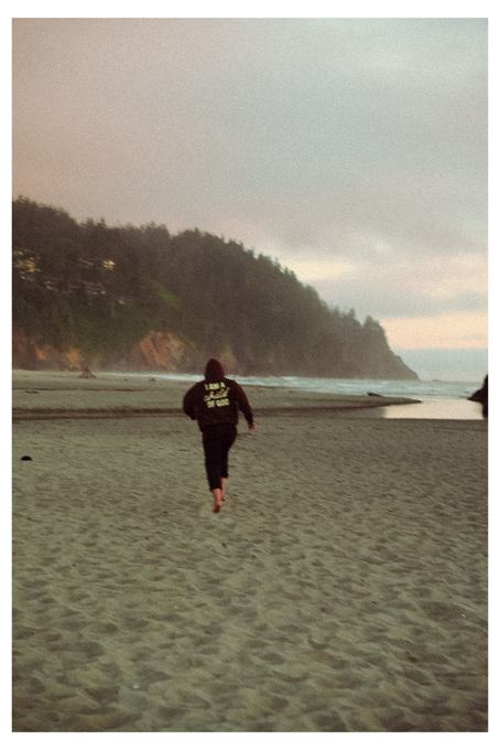 Person running barefoot down an Oregon beach at dusk in a hoodie
