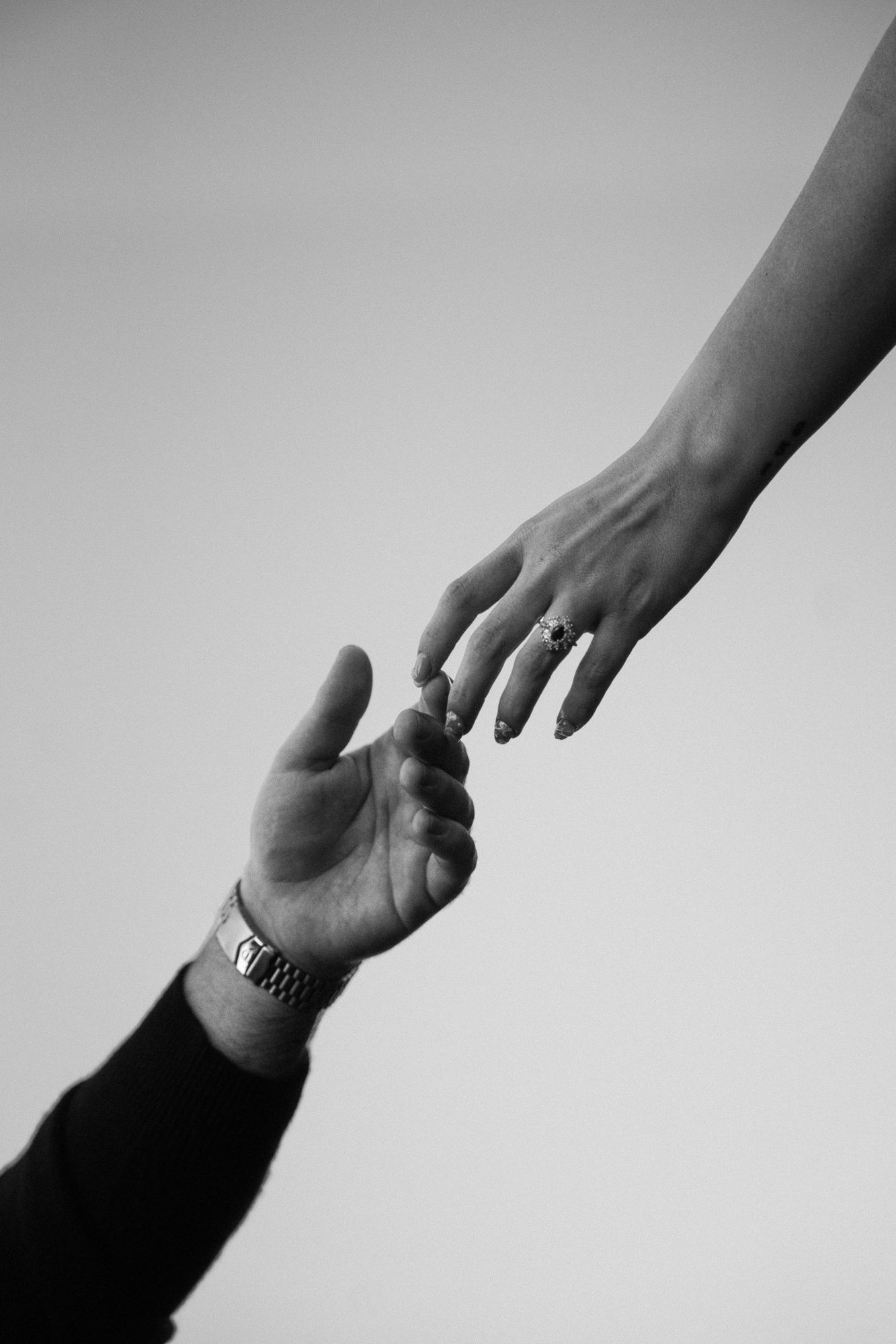 Black and white photo of James and Cora's hands reaching for each other against a soft gray sky