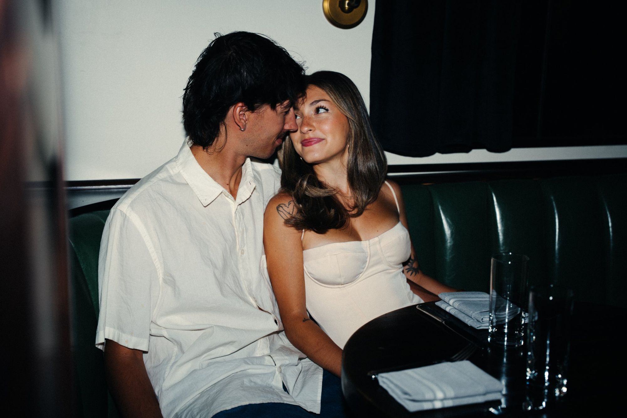 Lucas and Audry leaning close in a green leather booth, Audry looking up at him with a small smile