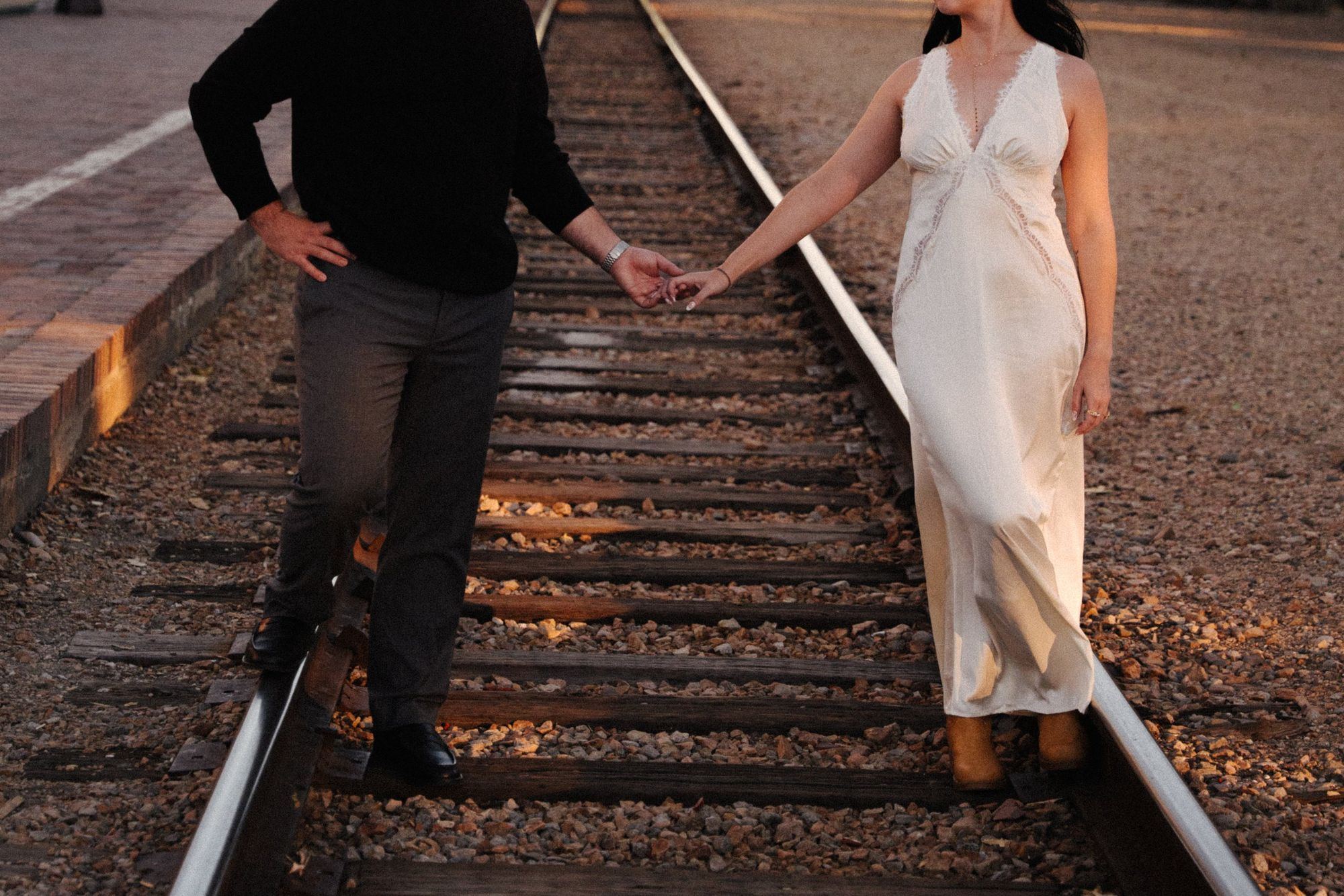 James and Cora walk toward each other holding hands on the railroad tracks near the Boise Depot in warm evening light