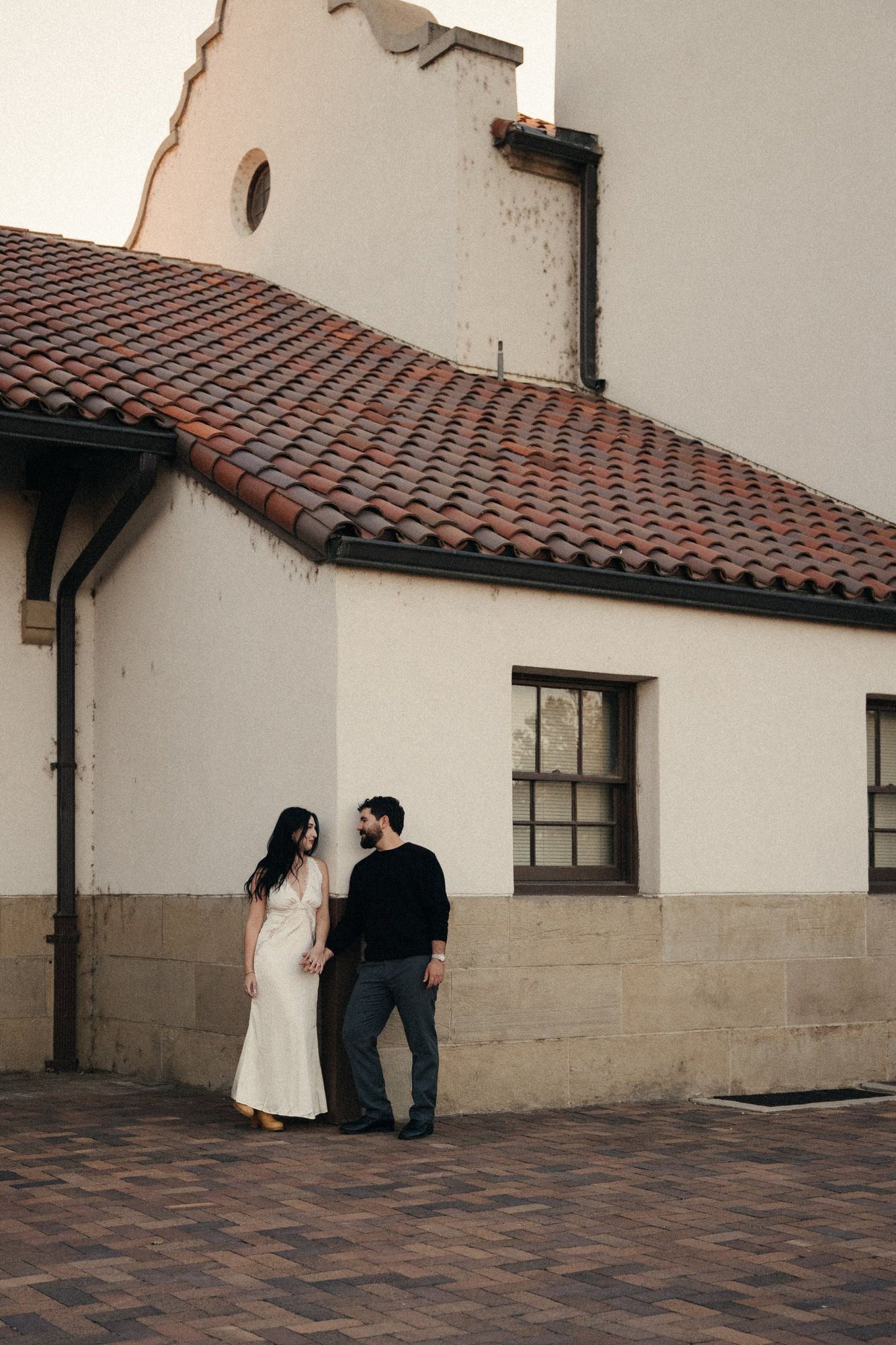 James and Cora standing hand in hand against a white stucco wall at the Boise Depot, under a red tile roof