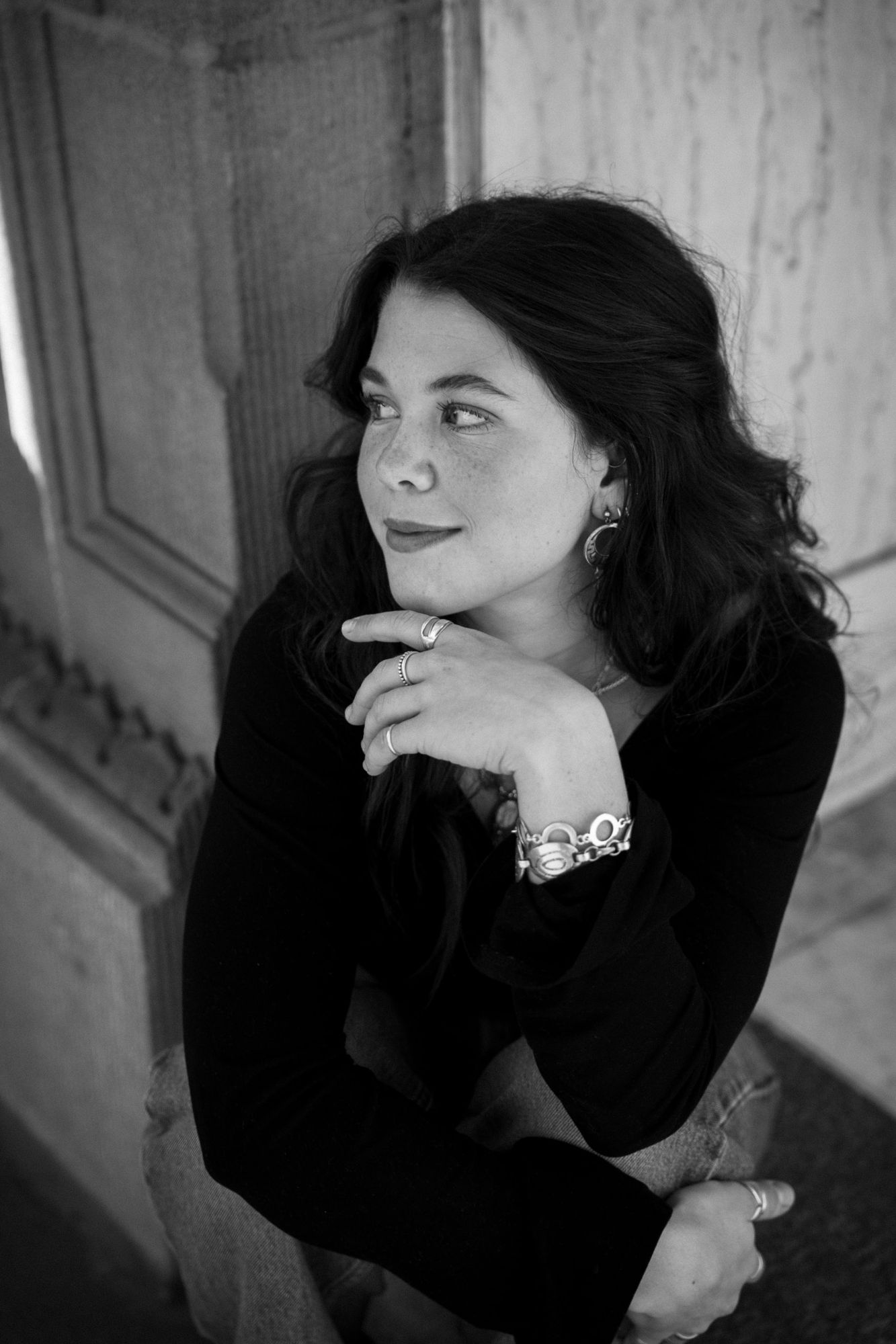 Adeline with a soft smile looking away from the camera in black and white, wearing silver rings and moon earrings