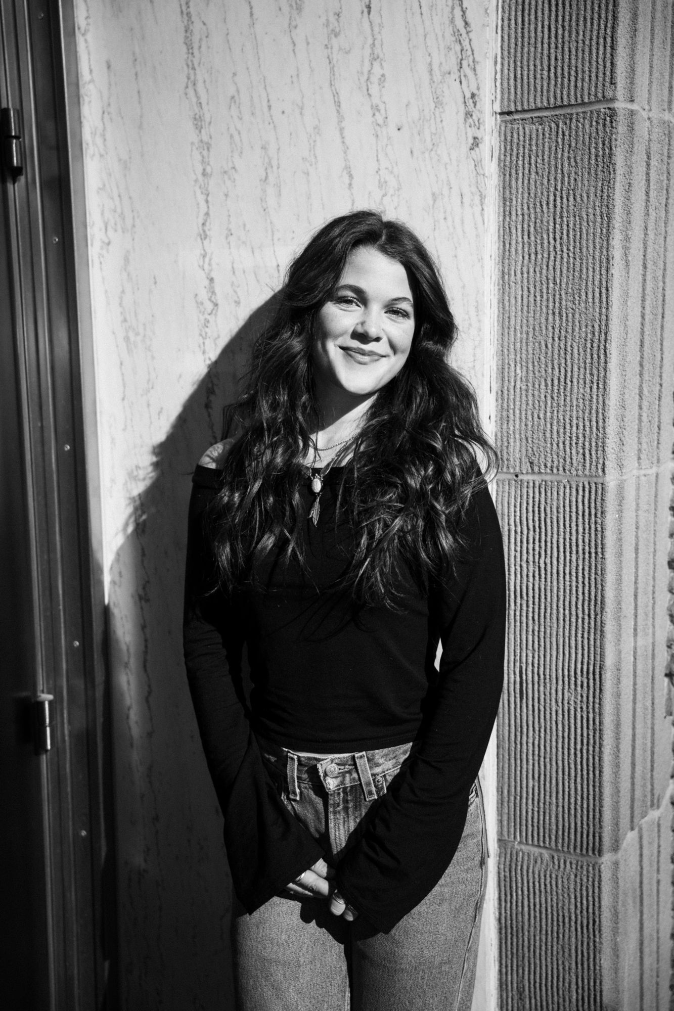 Adeline smiling at the camera in black and white, leaning against a marble wall beside a stone pillar