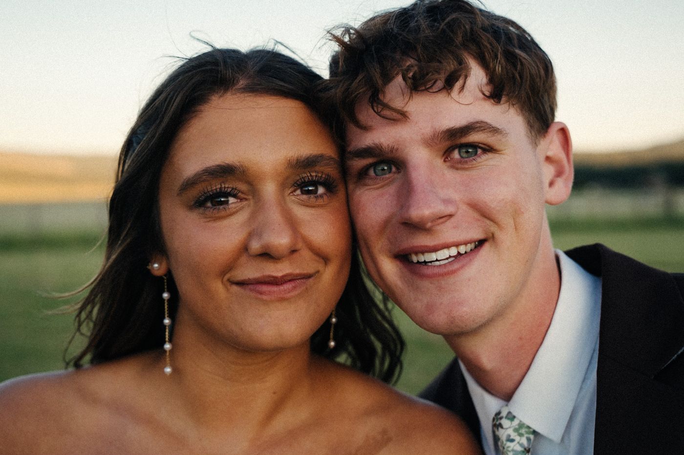 A bride and groom pressing their cheeks together and smiling at the camera in warm golden-hour light
