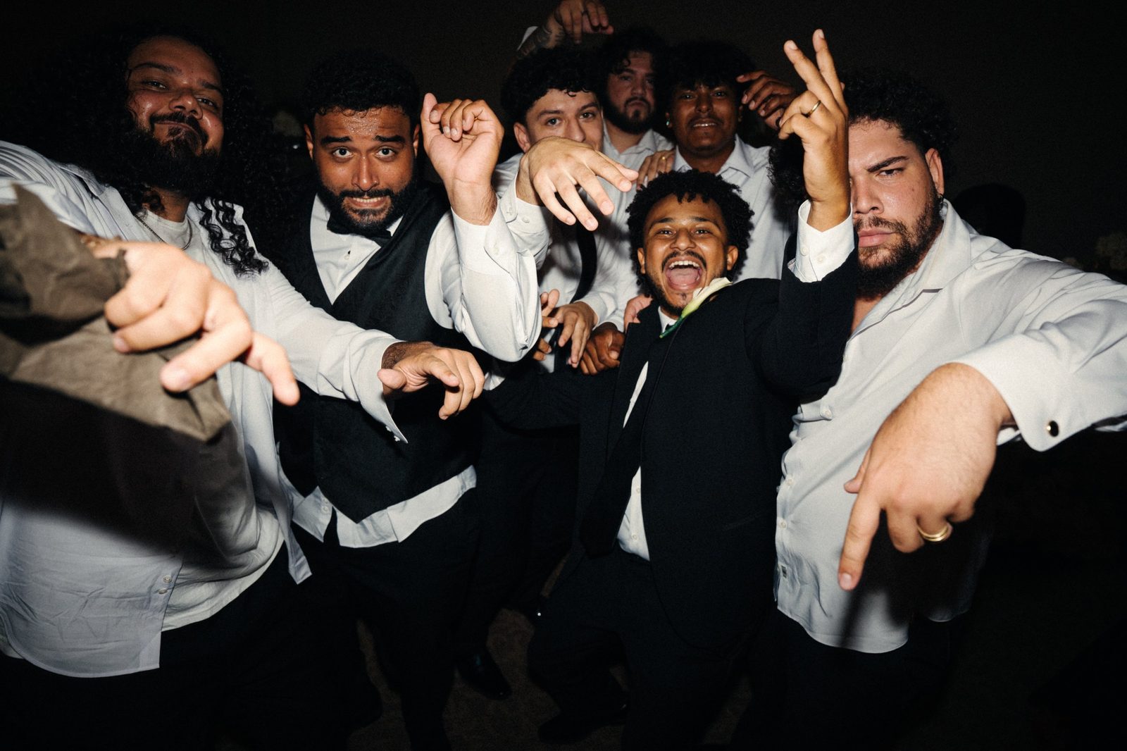 Caio and his groomsmen throwing hand signs and shouting together on the dance floor at the reception