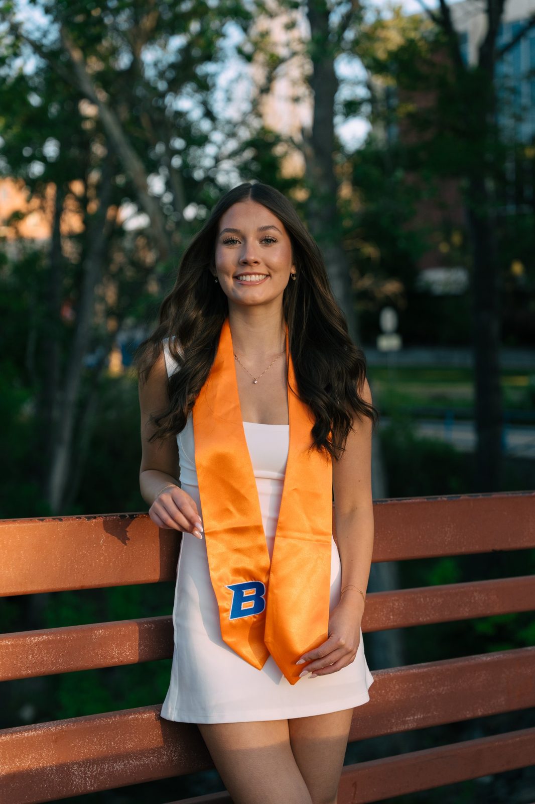 Charlotte leaning on a rust-red bridge railing with her orange Boise State stole in Boise, Idaho