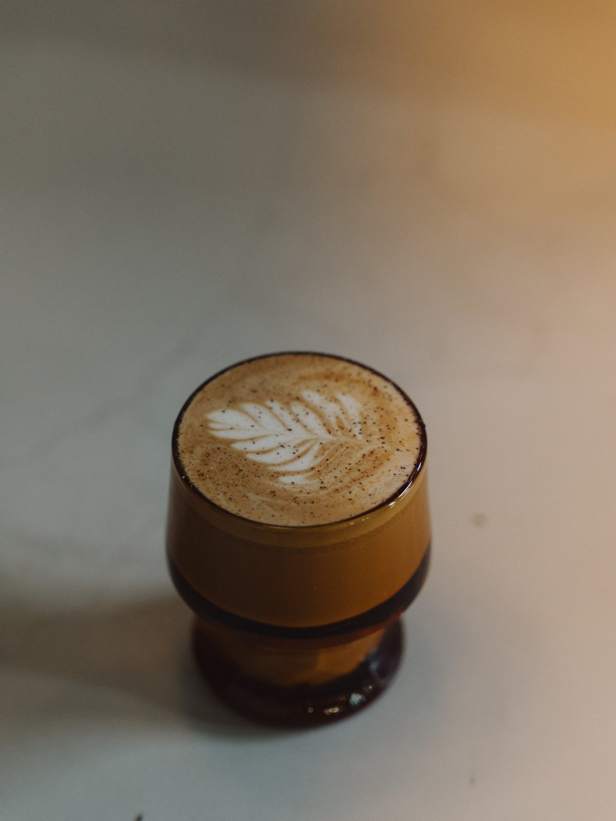 Latte with a leaf pattern in the milk, served in an amber glass