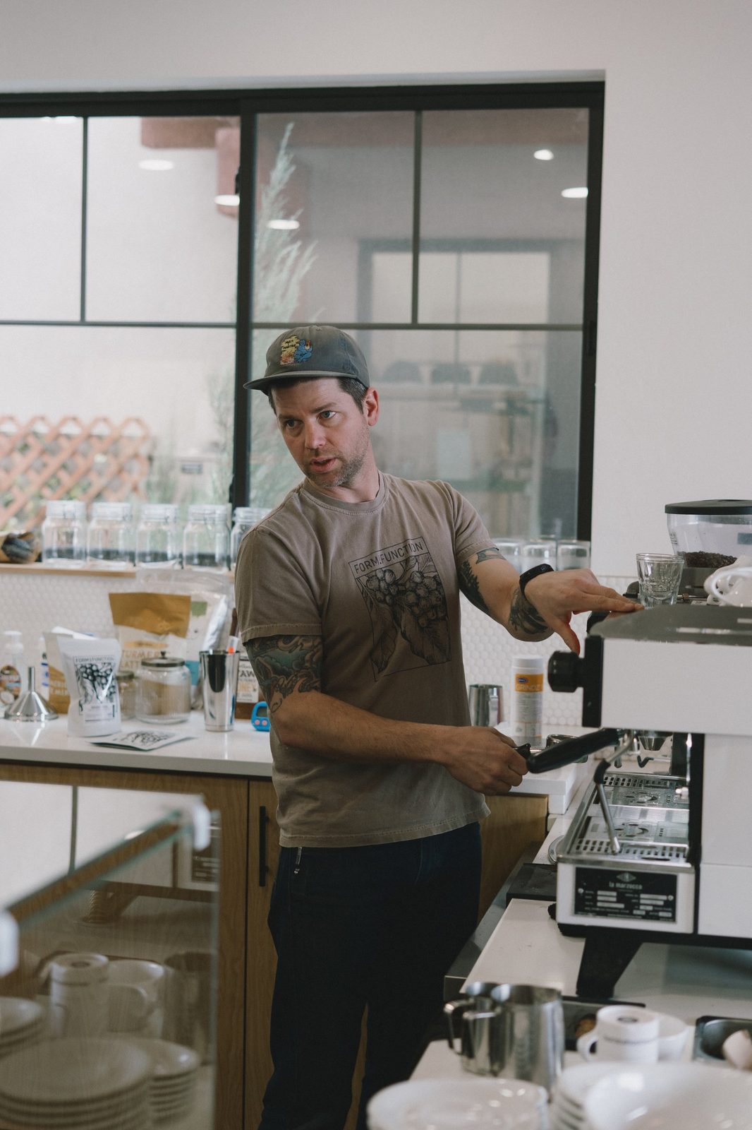 Barista in a cap and Form & Function t-shirt glancing to the side while working at the espresso machine