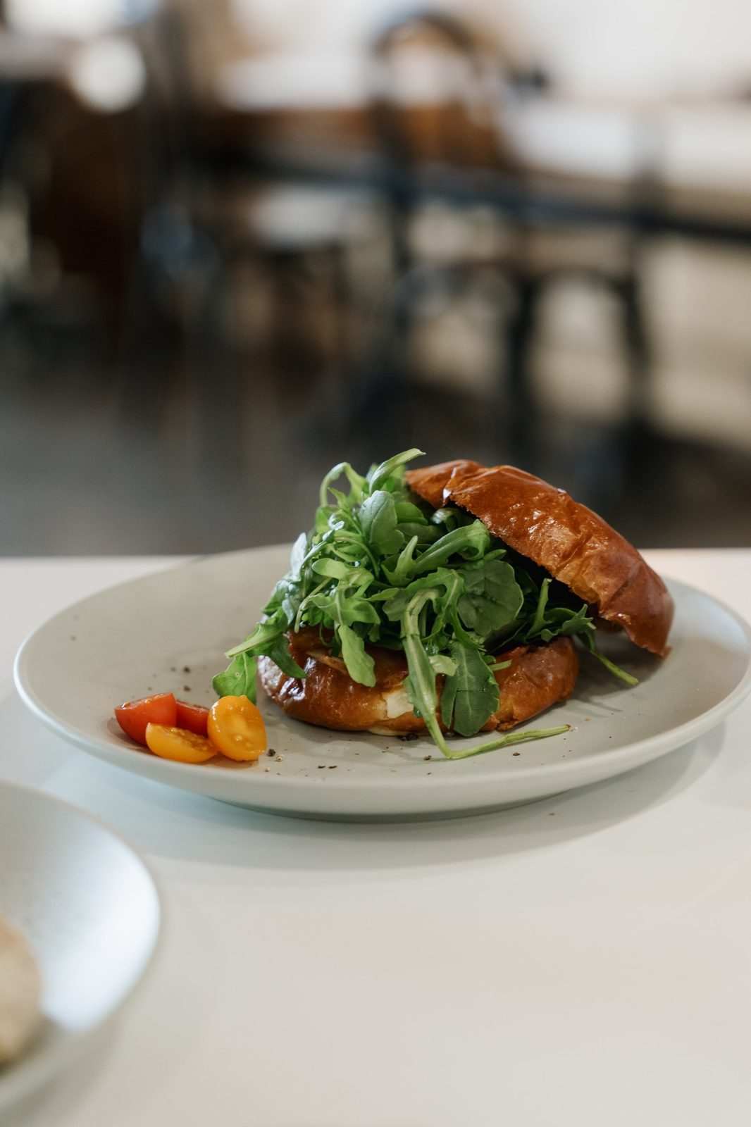 Brioche sandwich piled with arugula next to halved cherry tomatoes on a gray plate