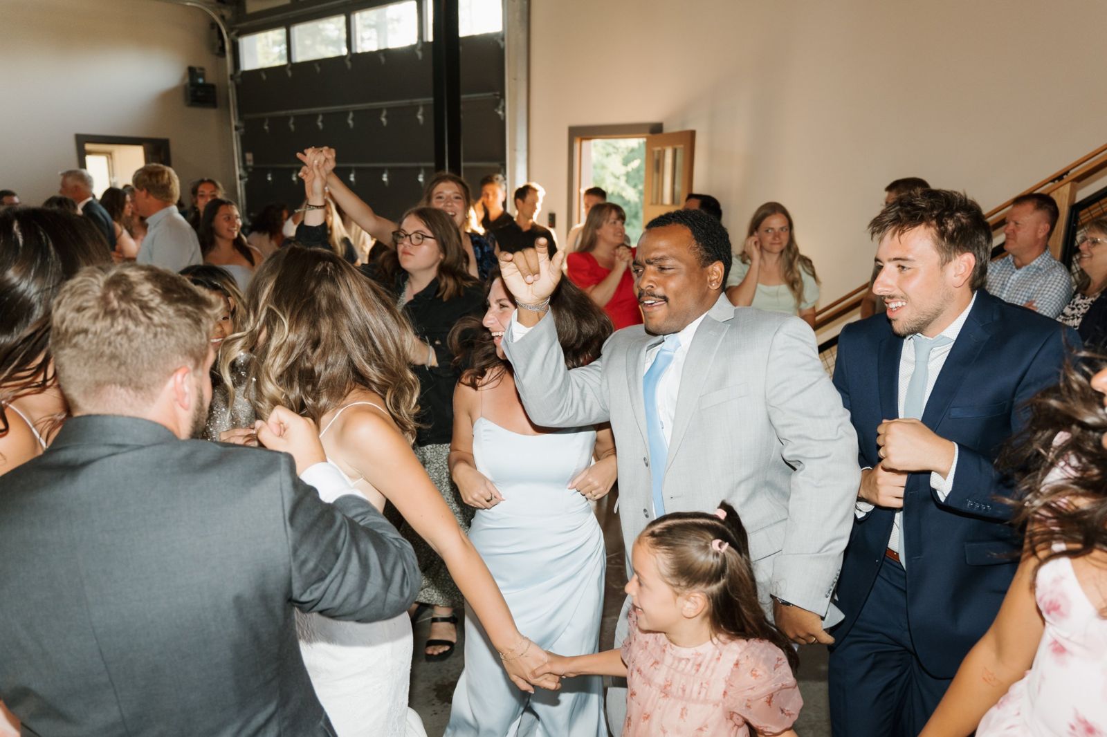 Wedding guests, the bride and a little flower girl dancing and laughing together on the reception dance floor
