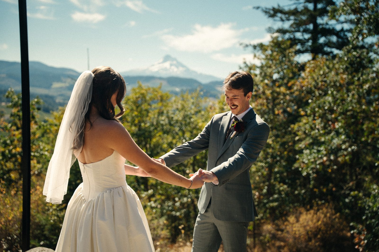 Bride and groom hold both hands during their first look, Mount Hood in the distance