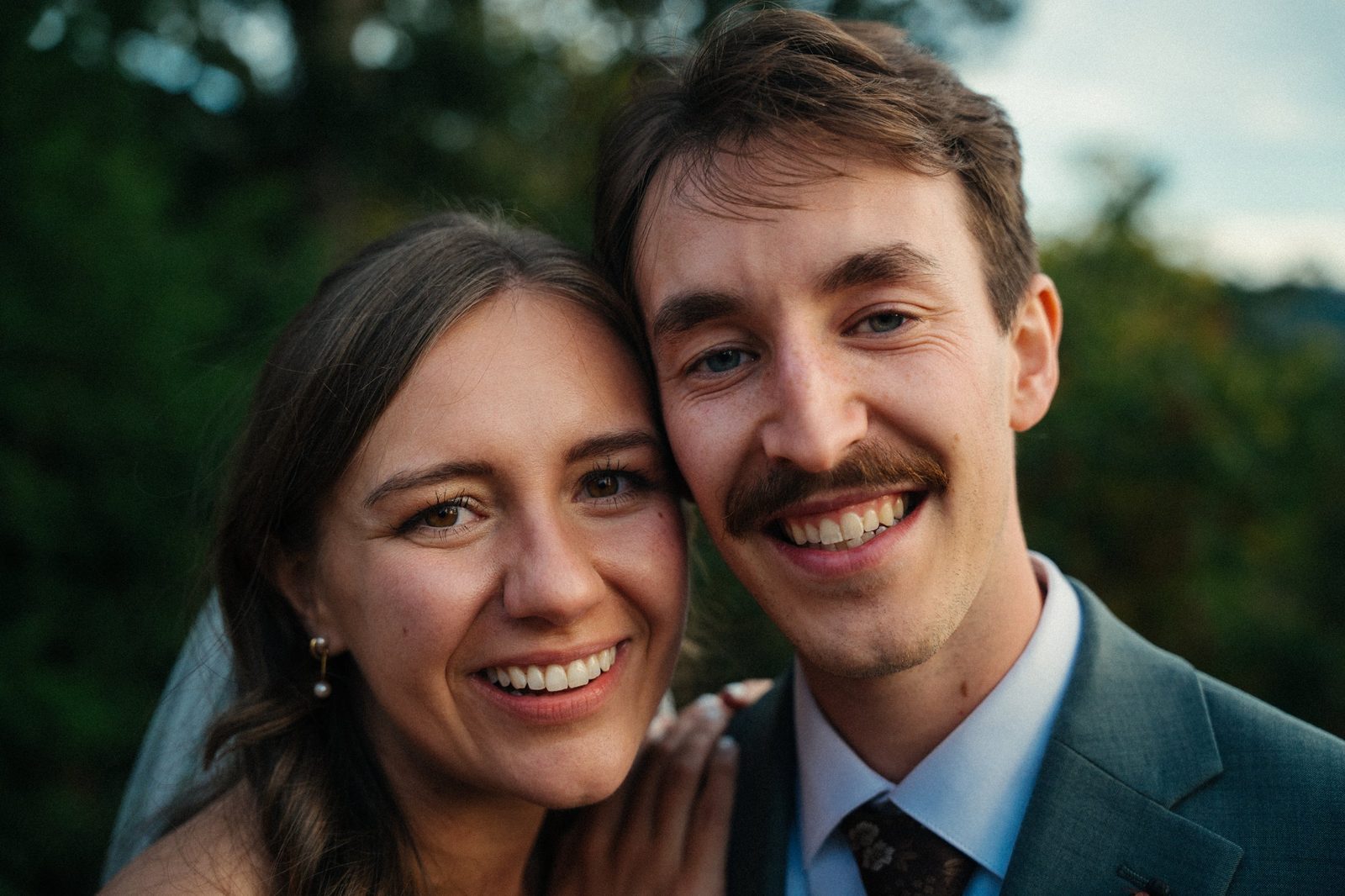 Bride and groom cheek to cheek, smiling right at the camera in warm evening light