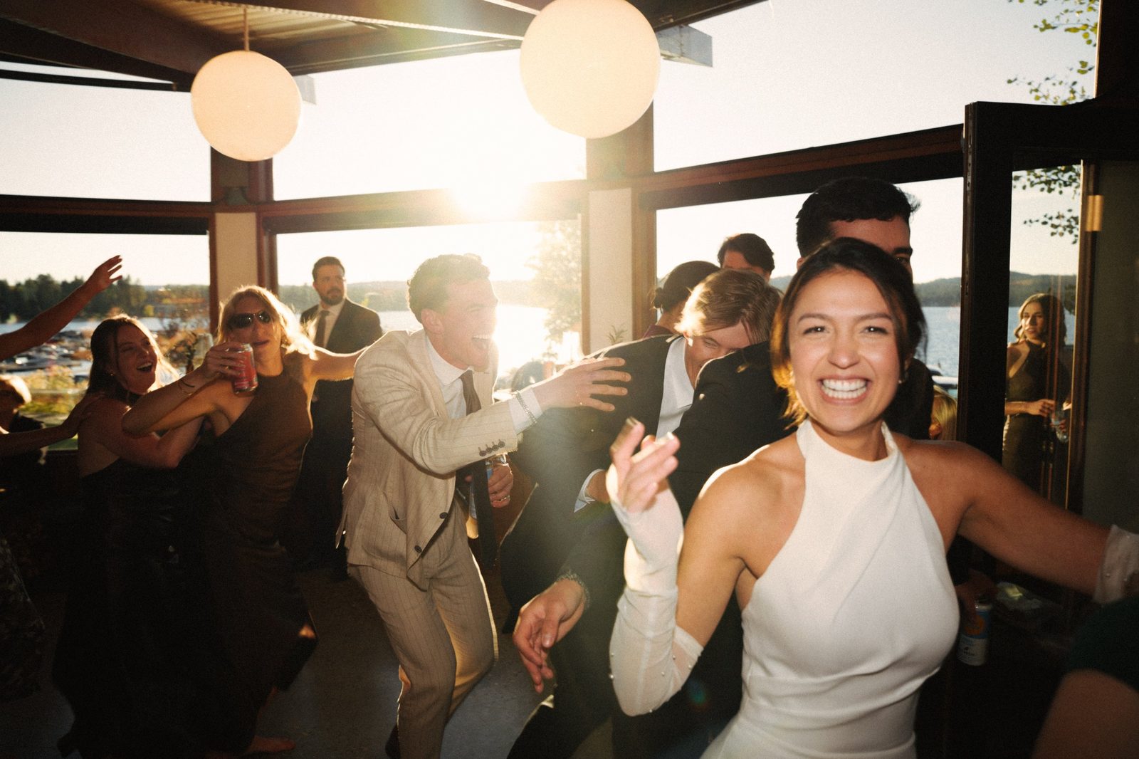 Becca laughing and dancing at the reception with guests behind her and the setting sun coming through the windows