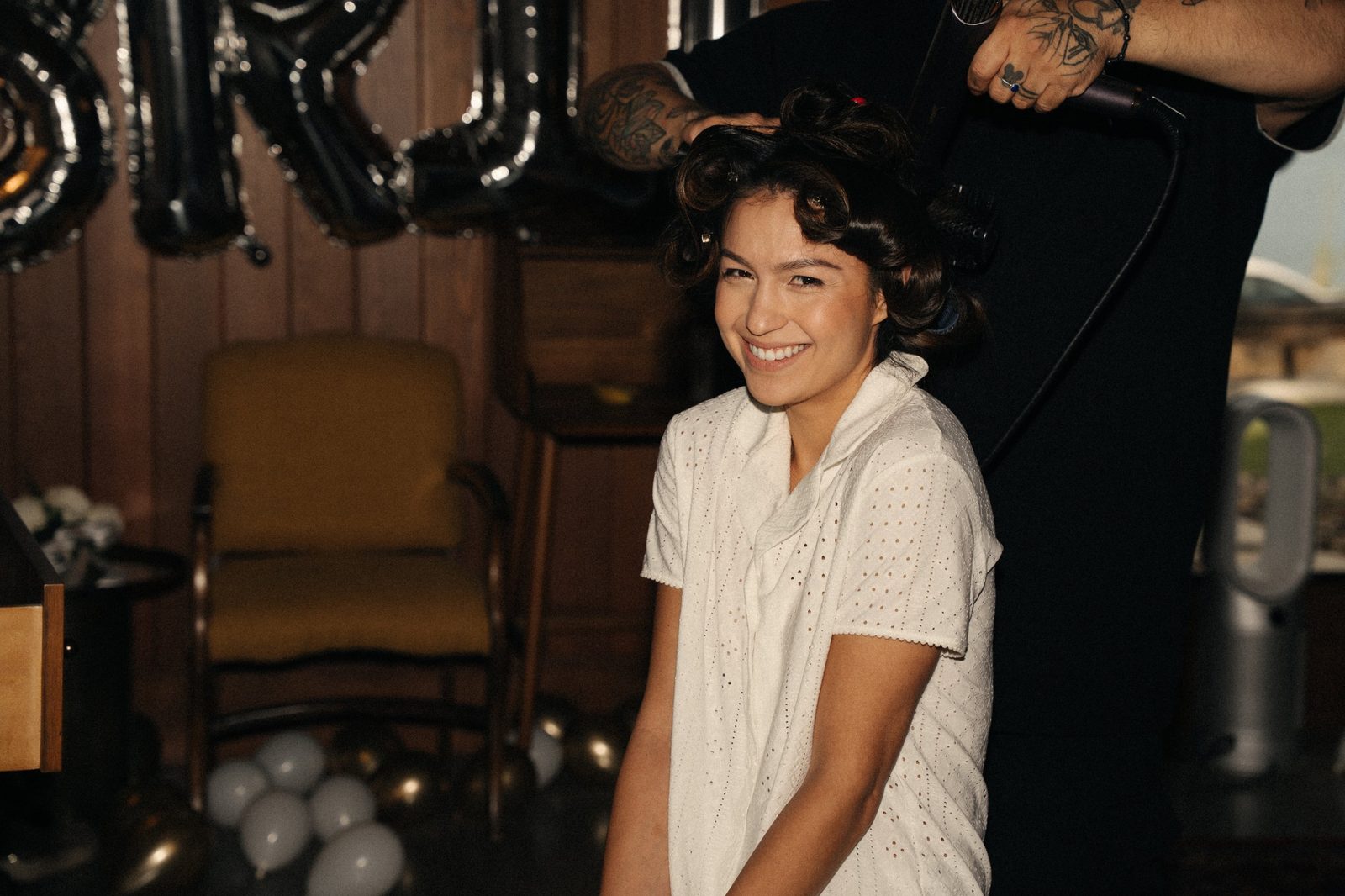 Becca smiling while her hair is curled and dried on the morning of her wedding in McCall, Idaho, with silver balloons behind her